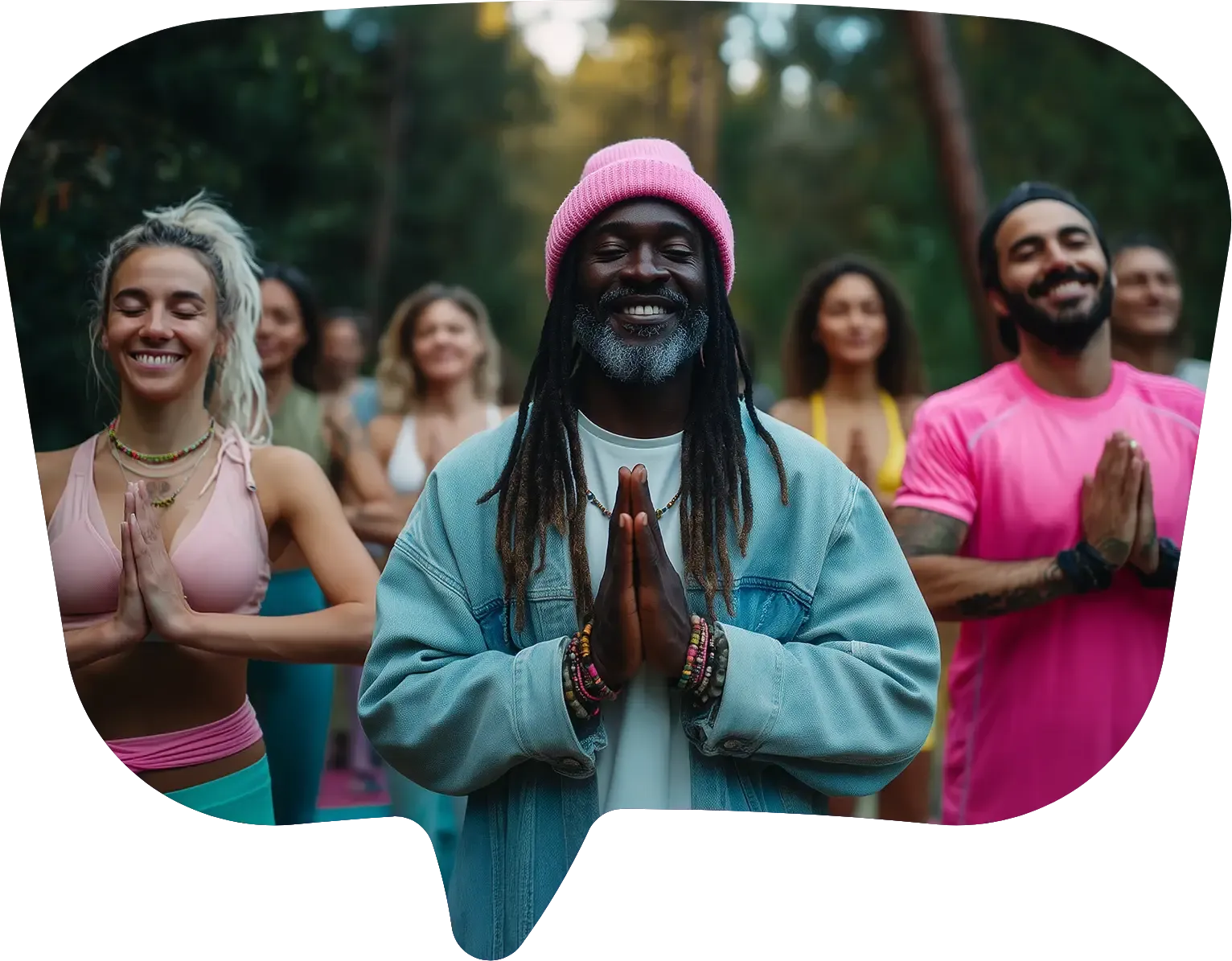 A group of people in bright activewear smile with palms pressed together in a forest