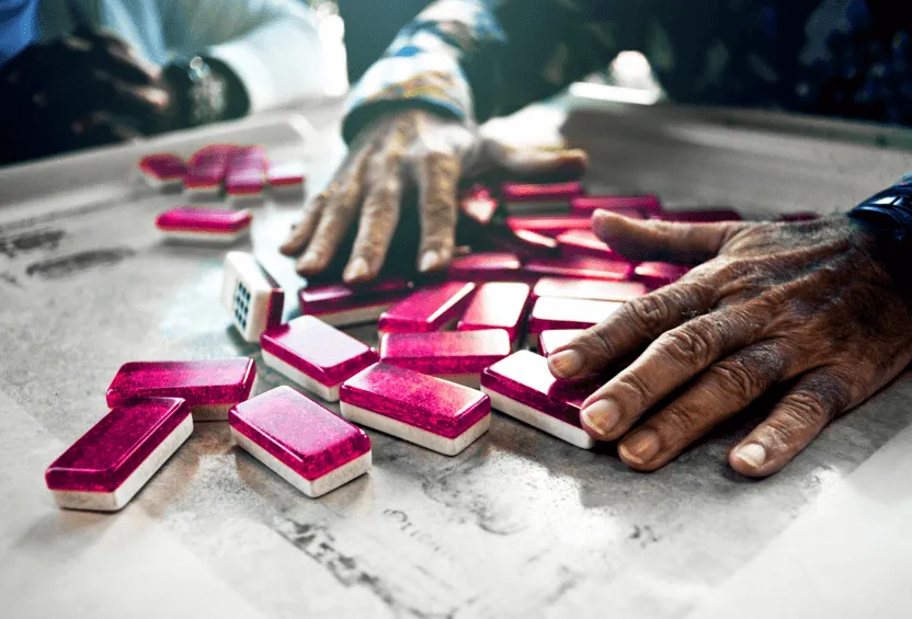 Unas manos mezclan fichas de dominó rosas y brillantes sobre una mesa